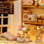 hand-assembled-tiny-cake-house-display-for-dessert-lovers Hand-assembled miniature bakery display featuring tiered cakes, fabric awning, and detail work