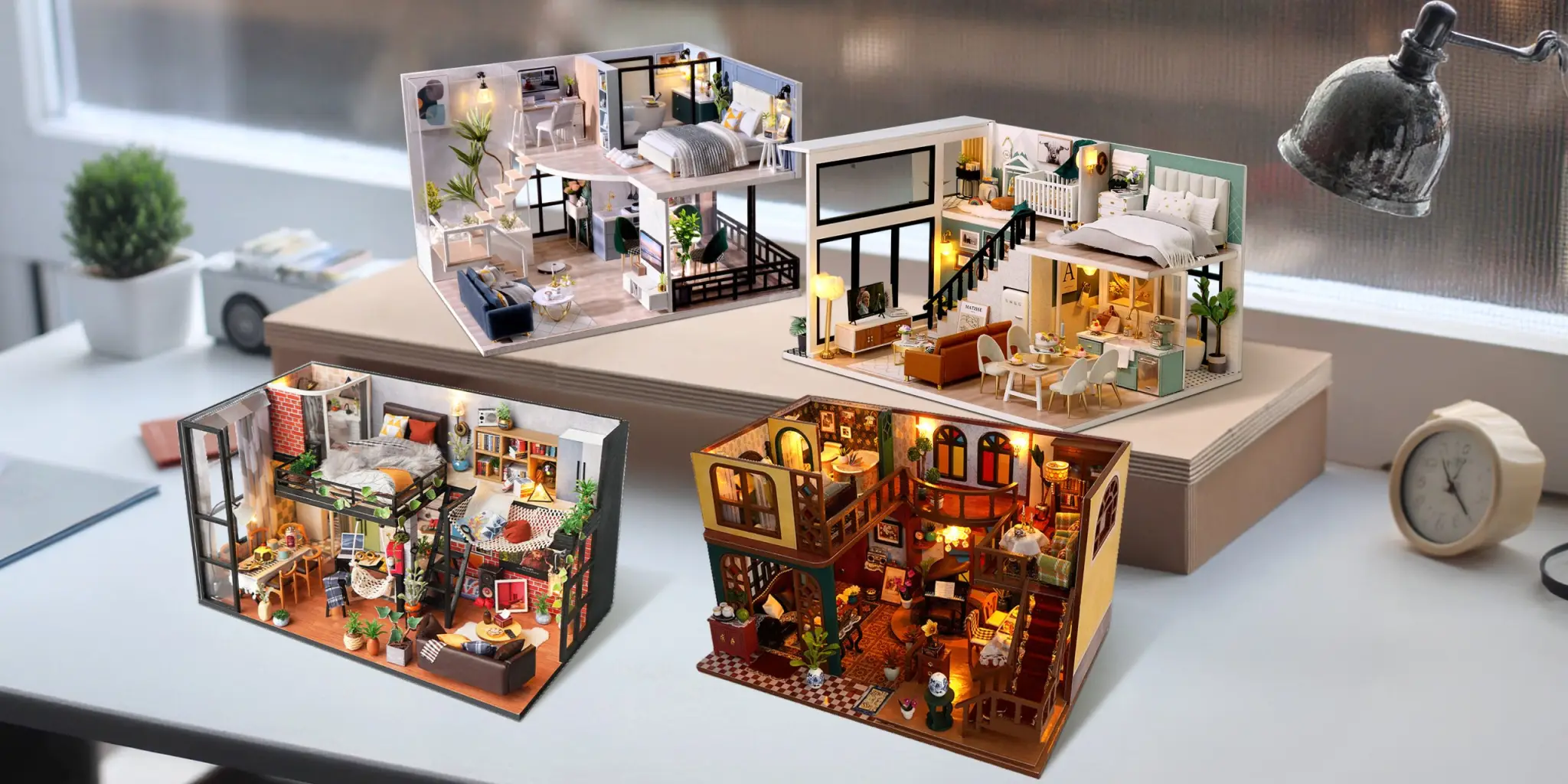 Four lit DIY miniature house kits displayed on a desk by a window